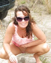  A woman in a pink top and sunglasses squatting down on the beach