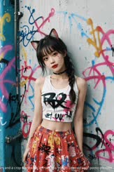 A young woman with cat ears and a crop top stands in front of a graffiti covered wall.