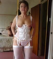 A woman wearing a white corset and stockings posing in front of a mirror.