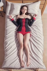 A woman with a slender body and a long hair in a black top and red underwear lying on the bed.